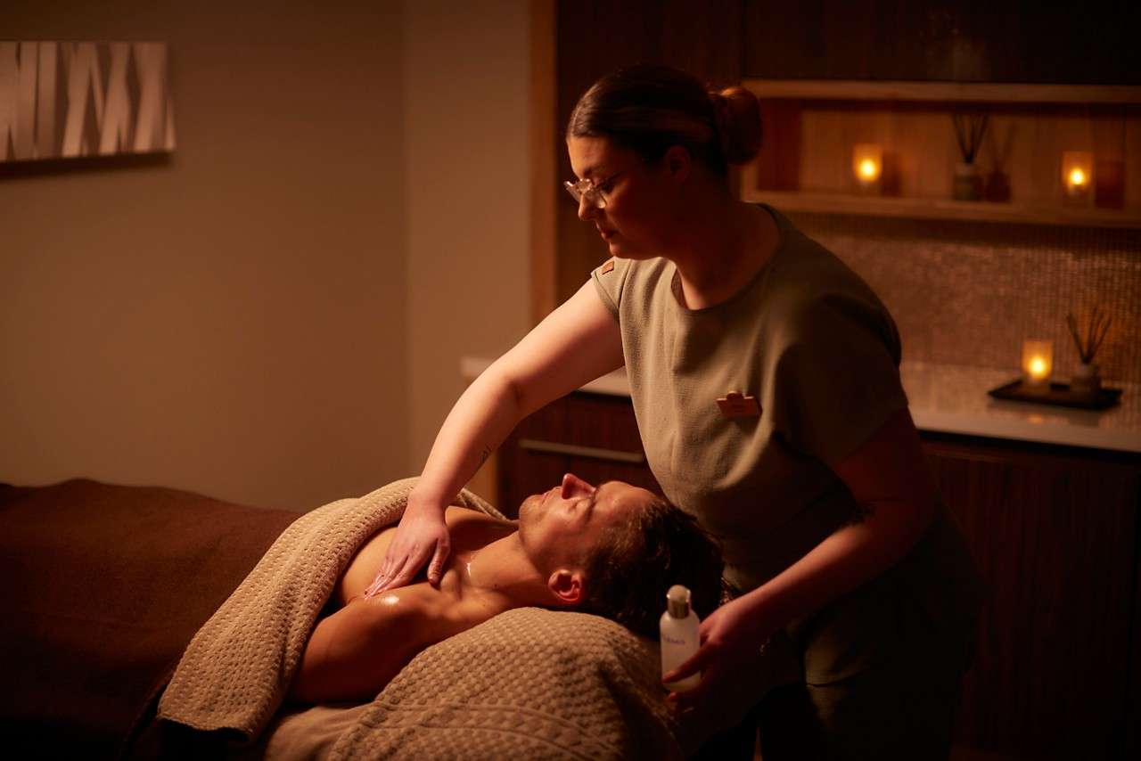 massage therapist rubbing oil on shoulder on client lying on a spa bed