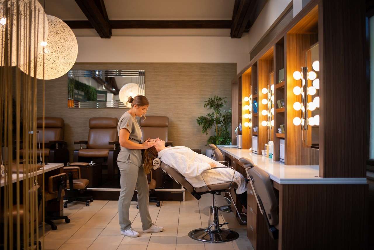 A therapist giving a facial treatment to a client in a spa robe reclining in a spa chair