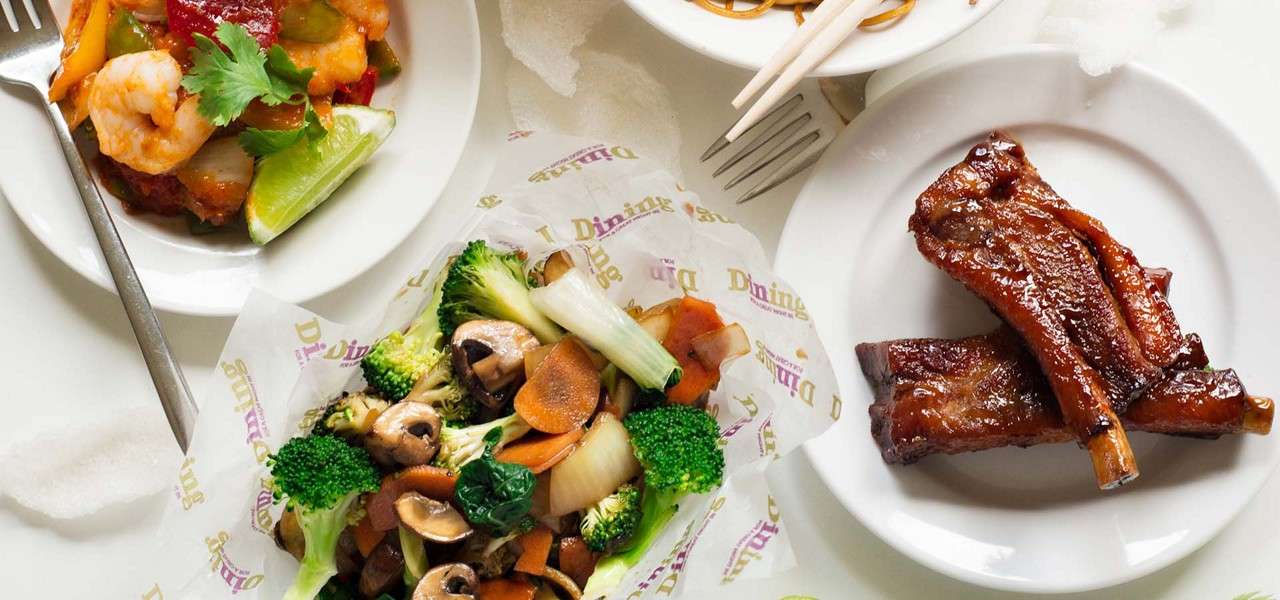 Dishes—glazed pork ribs, stir-fried broccoli, mushrooms and carrots, shrimp with peppers, and noodles—rest on white plates with chopsticks on a tabletop; wax paper shows text: “Dining” (repeated).