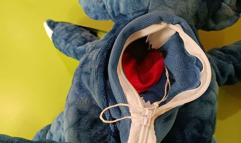 Blue stuffed animal reveals red heart through opened back zipper, with string ties, resting on a lime-green surface.