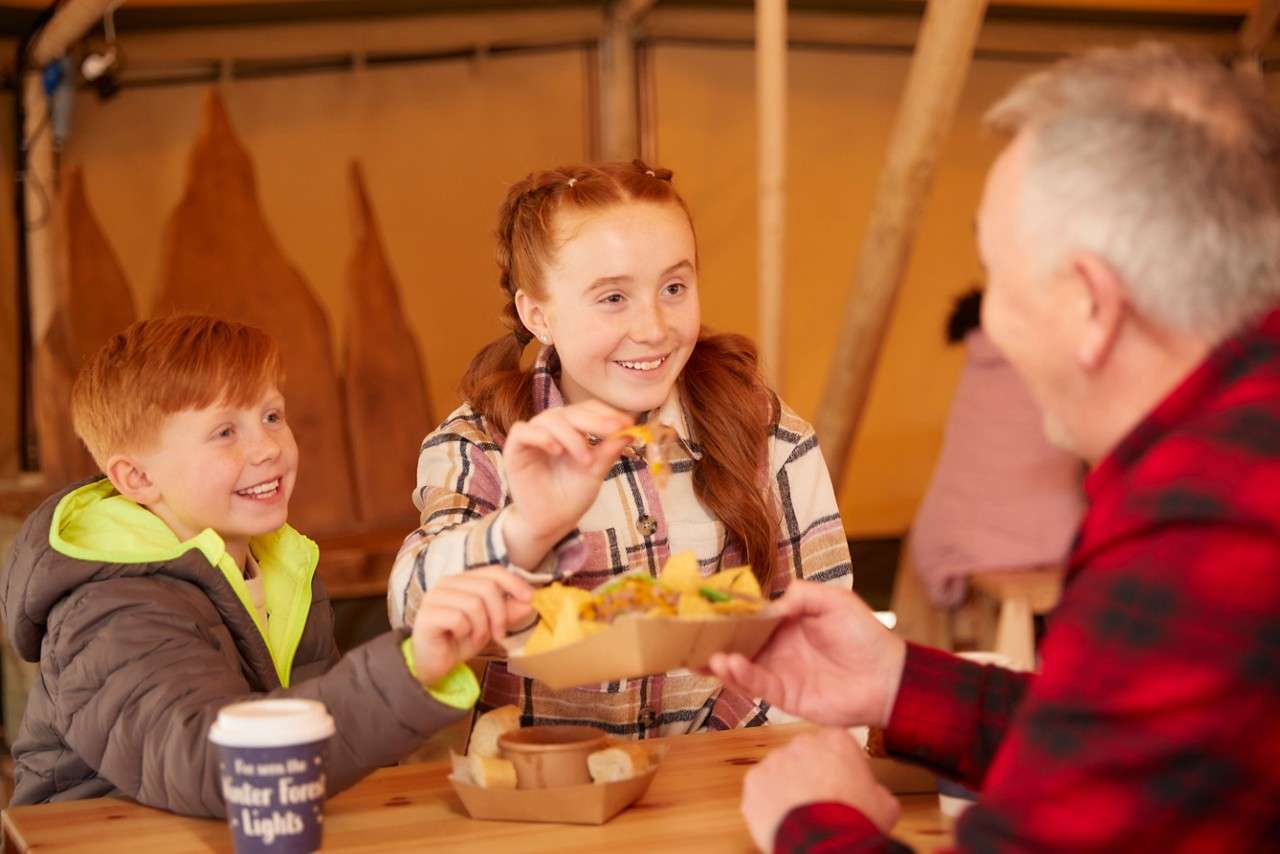 Family sharing loaded fries inside a tipi.