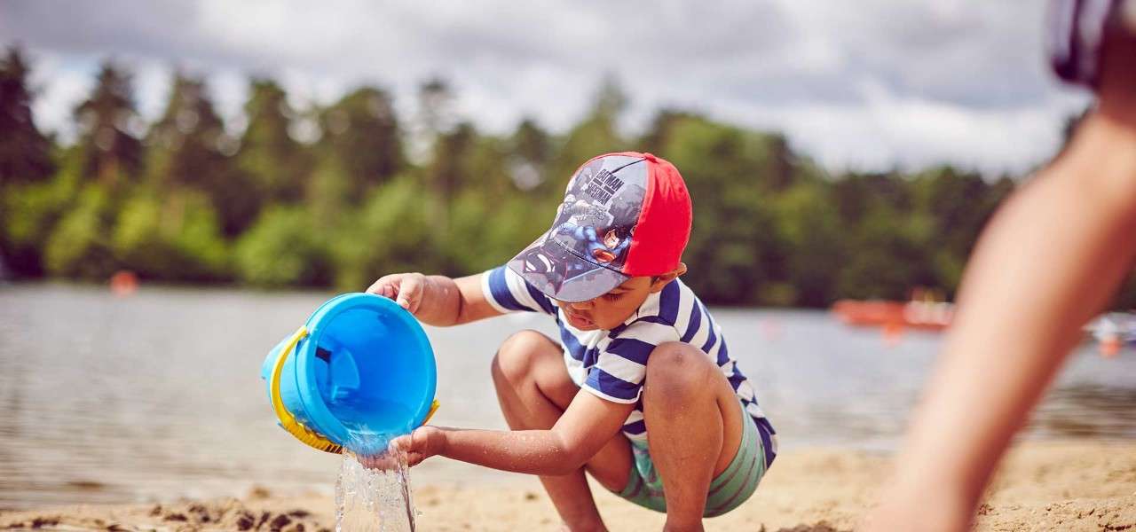Little boy playing on beach pouring water out his bucket
