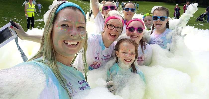 Group of staff at fundraising event covered in foam wearing matching Together for Short Lives charity t-shirts