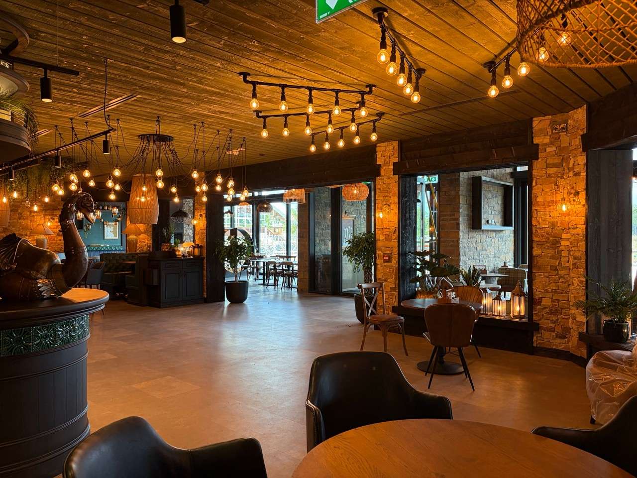 Warmly lit interior of The Swan's Lookout featuring exposed wooden ceilings, industrial pendant lighting, stone pillars and cosy seating