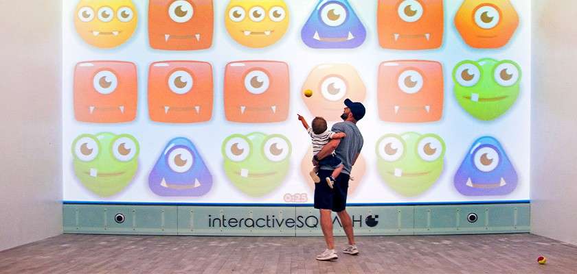 A father and his son stoof in front of the interactive squash board