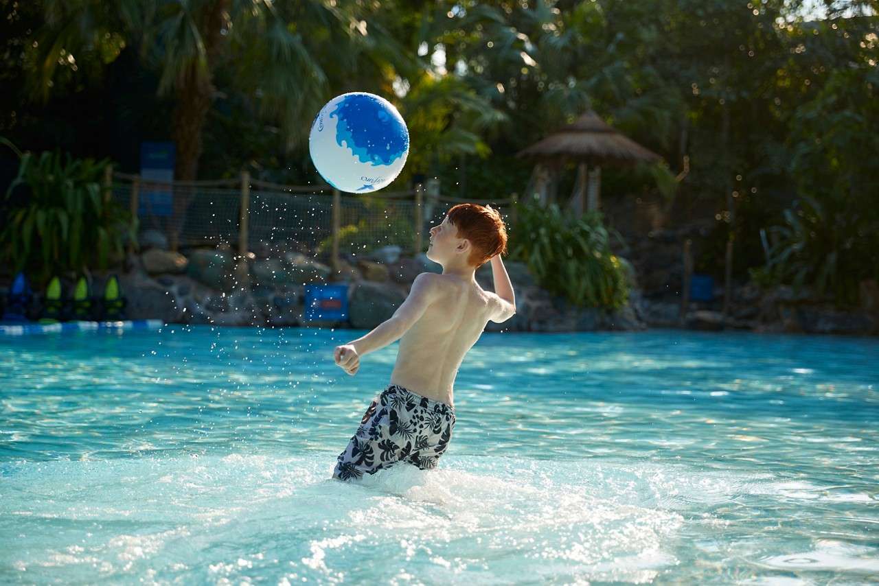 Four glasses of champagne on a light blue table decorated with twinkling lights and bronze leaf decorations. Bottle of champagne sits on the table in background. Two glasses are in focus in the dark room.