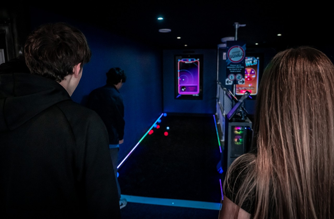 Two people playing a game of bowls in a dimly lit room with glow in the dark equipment. 