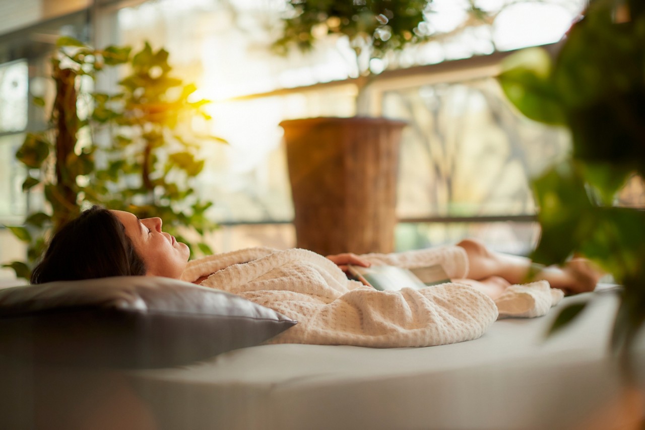 Woman laid on a Waterbed in a serene area with lots of plants and natural light.